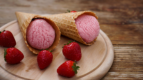 Strawberry ice cream in a waffle cone. Red berries and ice cream balls on a wooden background.