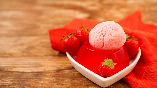 Strawberry jelly in a bowl, decorated with homemade ice cream. Wooden background and red napkin