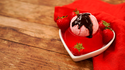 Strawberry jelly in a bowl, decorated with homemade ice cream and chocolate. Wooden background and red napkin