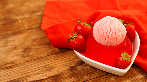 Strawberry jelly in a bowl, decorated with homemade ice cream. Wooden background and red napkin
