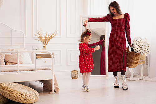 Mom and little daughter in red dresses in a bright bedroom in a Scandinavian style. Happy family. Mom holds a bouquet of daisies - spring photo