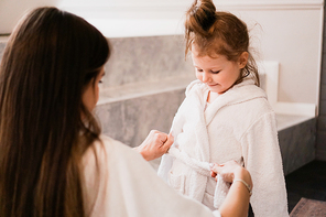 Mom puts her daughter in a white bathrobe in the bathroom. Happy family.