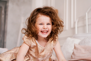 Portrait of a happy three-year-old girl. The blonde-haired child laughs. She is dressed in a beautiful beige dress for a children's party.