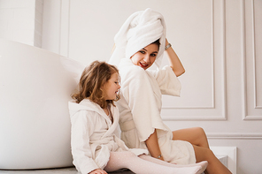 Mother and daughter in white coats in a light bathroom. Hygiene, beauty and happy family concept