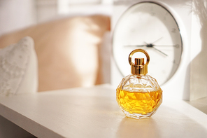 A bottle of yellow perfume on the night table. Against the background of a blurry clock.