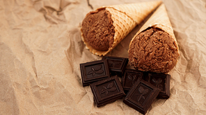 Chocolate ice cream in a waffle cone on craft paper background. Pieces of dark chocolate
