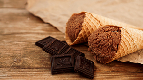 Chocolate ice cream in a waffle cone on craft paper on a wooden background. Pieces of dark chocolate