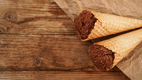 Chocolate ice cream in a waffle cone on craft paper on a wooden background. Two homemade ice cream