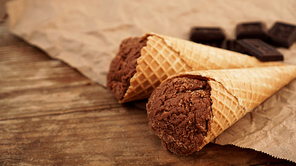 Chocolate ice cream in a waffle cone on craft paper on a wooden background. Pieces of dark chocolate