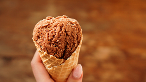 Chocolate ice cream on waffle cone in a woman hand. Wood background. Selective focus.