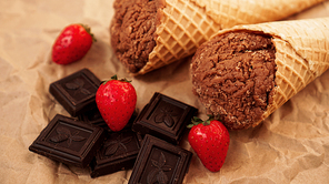 Chocolate ice cream in a waffle cone on craft paper background. Pieces of dark chocolate and strawberries