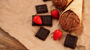 Chocolate ice cream in a waffle cone on craft paper background. Pieces of dark chocolate and strawberries