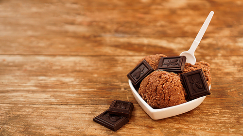 Homemade chocolate ice cream with chocolate pieces in a white bowl. Wooden background