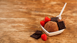 Chocolate ice cream in a bowl. Dessert decorated with chocolate and strawberries. Sweets on wooden background. White plastic spoon