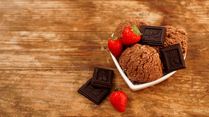 Chocolate ice cream in a bowl. Dessert decorated with chocolate and strawberries. Sweets on wooden background