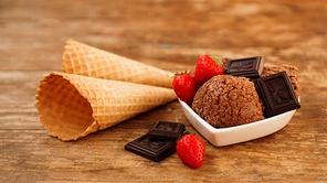 Chocolate ice cream in a bowl. Dessert decorated with chocolate and strawberries. Wooden background and two waffle cones