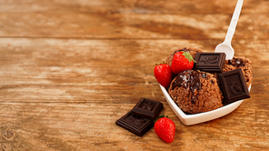 Chocolate ice cream in a bowl. Dessert decorated with chocolate and strawberries. Sweets on wooden background. White plastic spoon