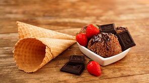 Chocolate ice cream in a bowl. Dessert decorated with chocolate and strawberries. Wooden background and two waffle cones