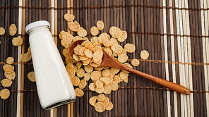 Healthy cornflakes and milk and a wooden spoon on a bamboo napkin. Glass bottle with milk for a healthy breakfast