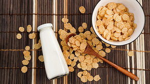 Healthy cornflakes and milk and a wooden spoon on a bamboo napkin. Glass bottle with milk for a healthy breakfast