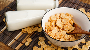 Healthy cornflakes and milk and a wooden spoon on a bamboo napkin. Glass bottles with milk for a healthy breakfast