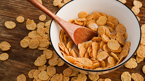 Yellow cornflakes in a white bowl. Wooden spoon in a bowl. The concept of healthy eating and delicious breakfast. Wood background