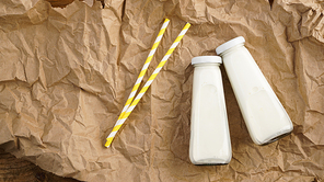 Organic cow milk in glass bottles. Two bottles of milk on crumpled craft paper. Two yellow paper drinking straws. Natural milk for health.