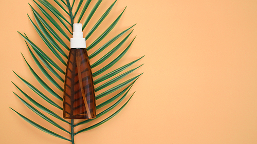 Suntan lotion bottle on soft orange background with tropical leaf. Top view, copy space. Sun protection cosmetic products, summer skin care concept