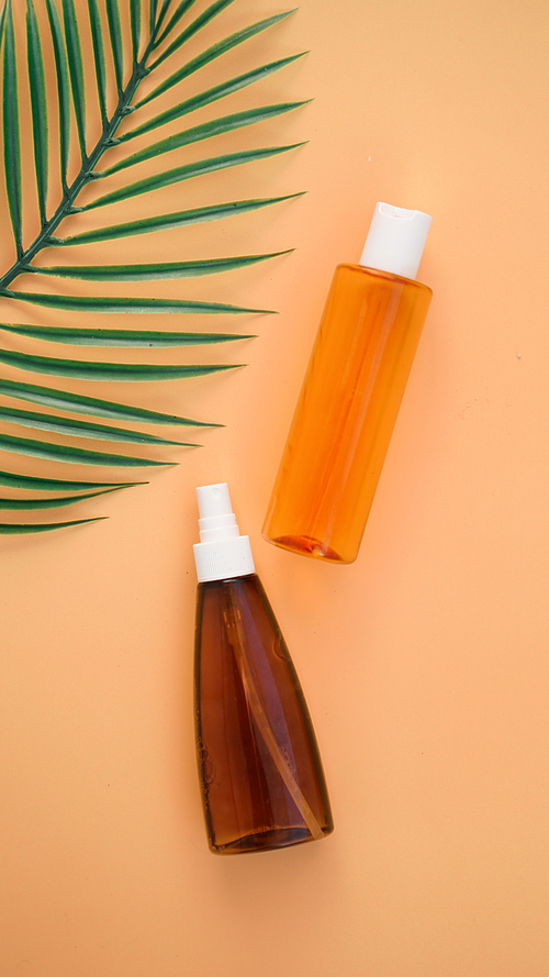 Suntan lotion bottle on soft orange background with tropical leaf. Top view, copy space. Sun protection cosmetic products, summer skin care concept