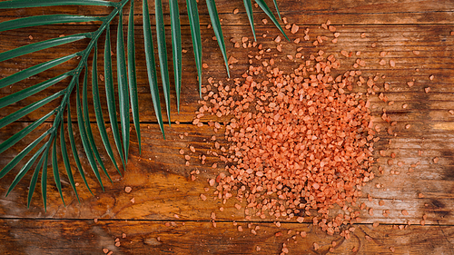 Orange sea salt on a wooden background. Tropical palm leaves on background. Beauty concept. Spa background with a space for a text