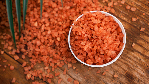 Orange sea salt on a wooden background. Tropical palm leaves on background. Beauty concept. Spa background with a space for a text