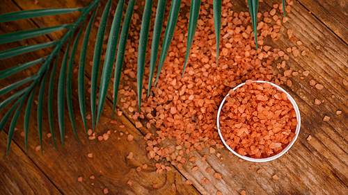 Orange sea salt on a wooden background. Tropical palm leaves on background. Beauty concept. Spa background with a space for a text. Selective focus