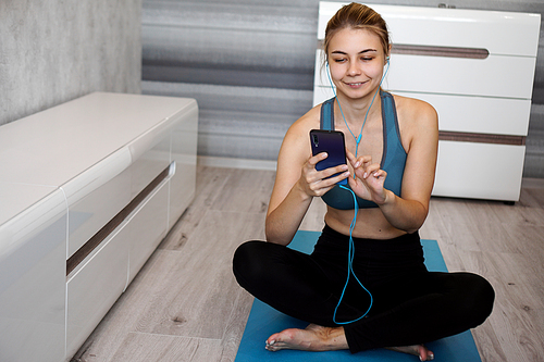 Take sport and add music. Female athlete with earphones enjoying the music playing and touching a screen of her phone while sitting on the floor.