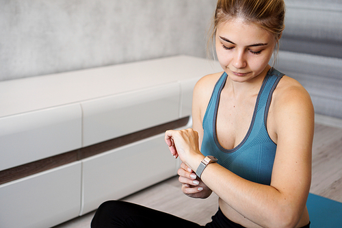 Portrait of young woman checking digital fitness tracker during self-training at home