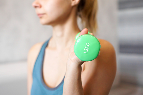 Sport and recreation concept - sporty woman hand with light green dumbbell