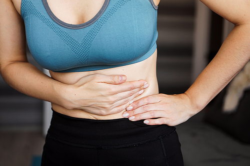 Close up of the woman holding her belly. Pain after home workout. Weight loss, slim body, healthy concept