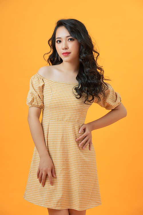Fashionable young beautiful model posing on yellow studio background wearing dress