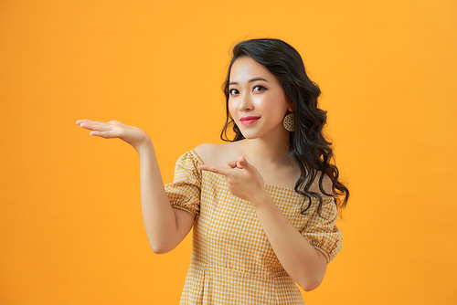 Beauty woman with charming smile and show something to you on yellow background, asian beauty