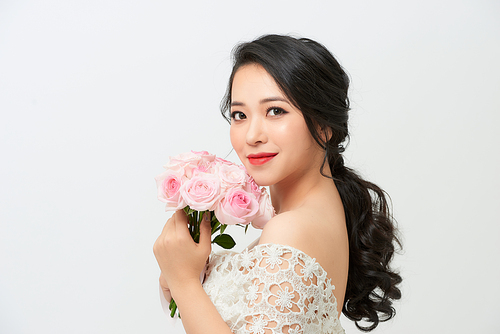 Young attractive Asian model like a bride with bridal bouquet at studio looking
