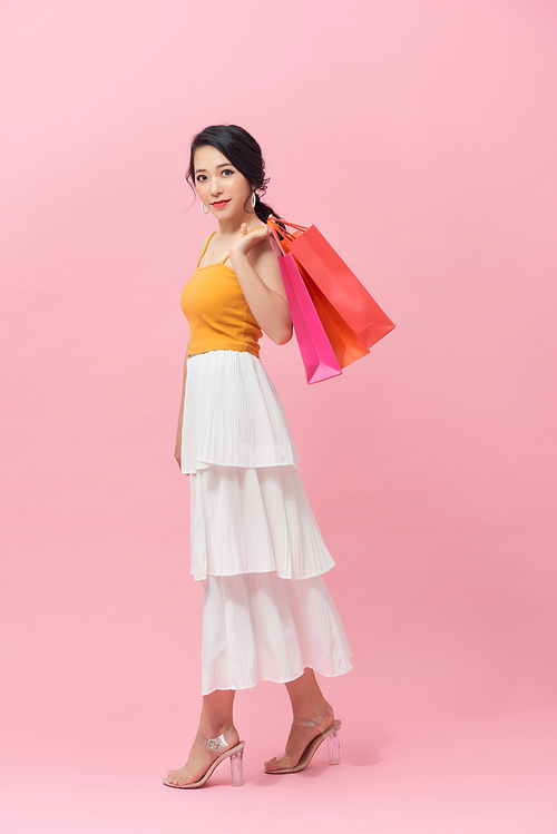 full length view of cheerful, fashionable woman holding colorfull shopping bags and smiling on pink background