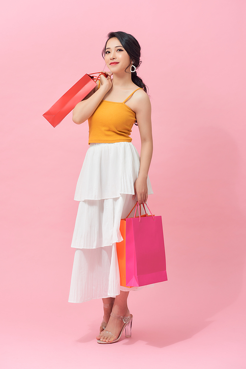 Full length portrait of a beautiful young woman posing with shopping bags, isolated against pink background