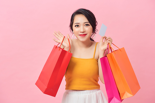 Portrait of a beautiful girl wearing dress and holding colorful shopping bags and showing credit card isolated over pink background