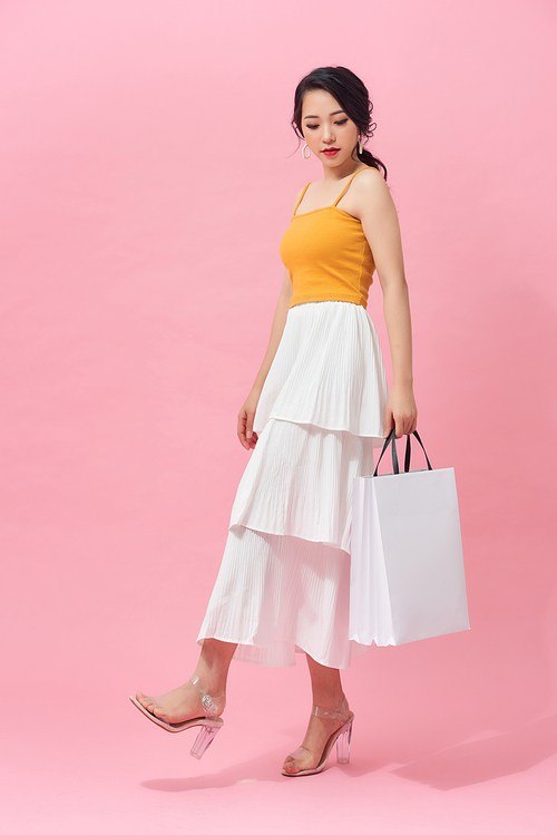 Full length side view of young woman walking with shopping bag isolated over pink background