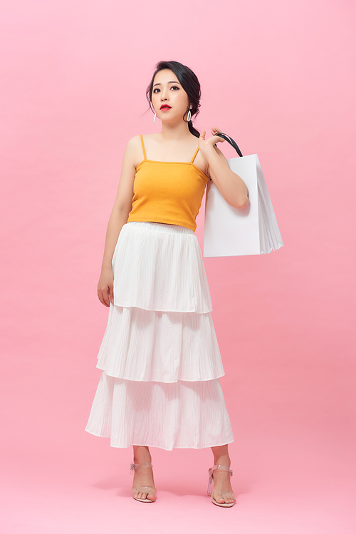 Full length portrait of smiling young woman with shopping bags over pink background.
