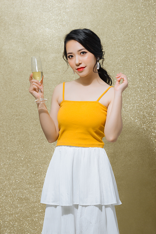 Portrait of beautiful young Asian woman holding wine glass over gold background. Celebrating concept.