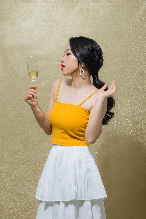 Beautiful young Asian woman raising wine glass over gold background. Party concept.