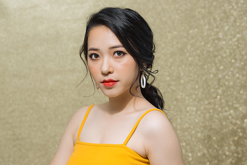 Portrait of attractive young Asian woman over gold background.