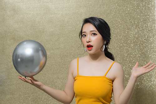 Cheerful young Asian woman with balloons laughing over gold background.