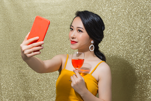 Party time. Beautiful young Asian woman making selfie on the phone in party glasses.