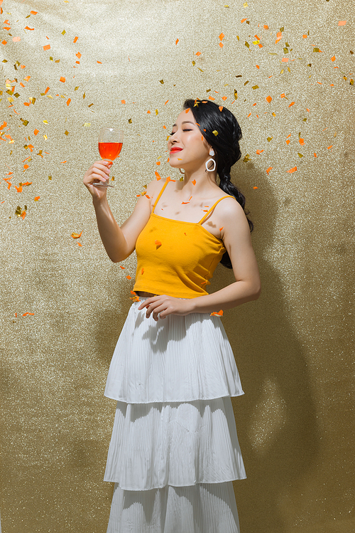 Beautiful young woman with confetti, celebration  with glass of champagne over gold background.